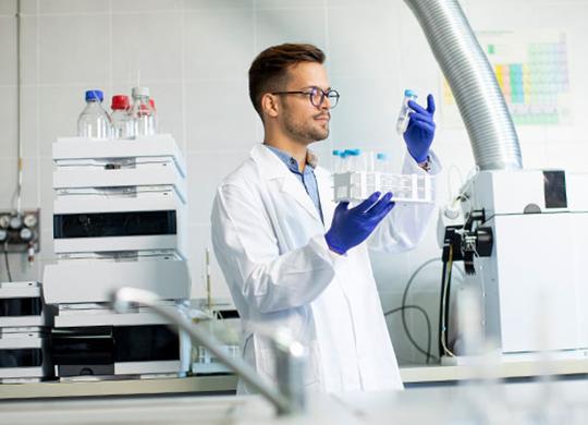A scientist wearing a white lab coat and glasses holds and examines chromatography columns.png A scientist wearing a white lab coat and glasses holds and examines chromatography columns.png