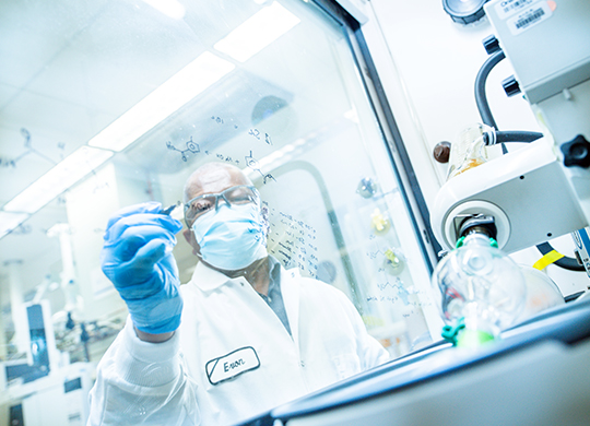 Masked scientist wearing white coat and blue gloves writing notes on a glass board in a mAbs research lab